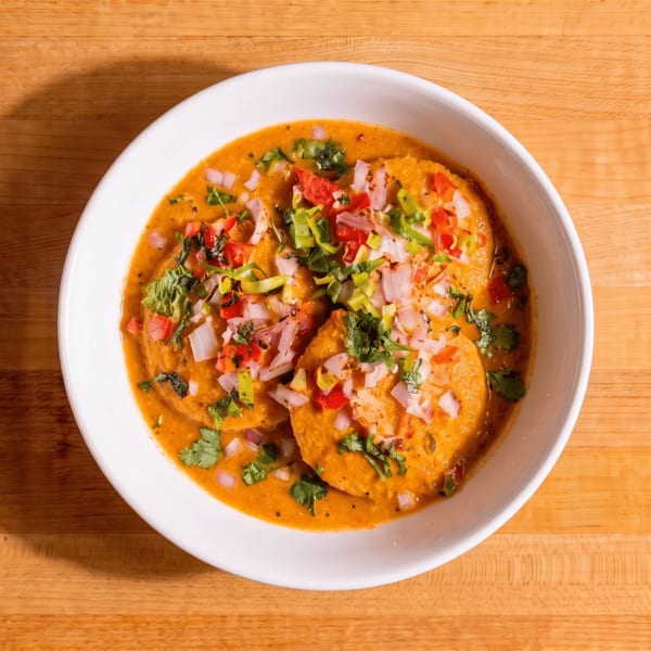 Savory pancakes in a rich orange sauce, topped with diced red onions, tomatoes, and green herbs.