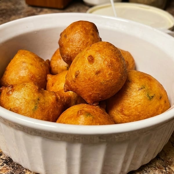 A white bowl filled with golden-brown, round fried dough balls, possibly puff-puffs or similar fritters.
