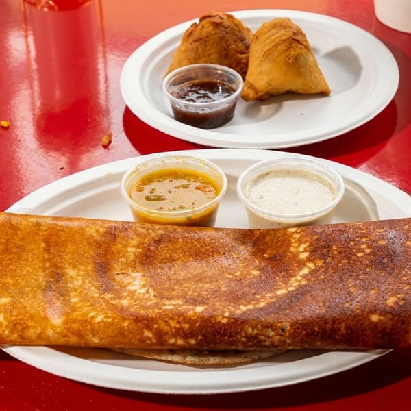 A dosa with two dipping sauces and two samosas with chutney on a red table.