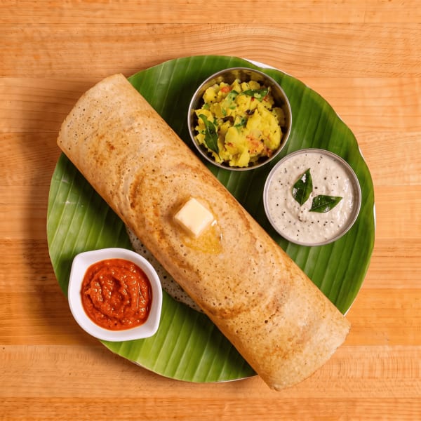 Dosa with a pat of butter, served on a banana leaf with potato masala, coconut chutney, and sambar.