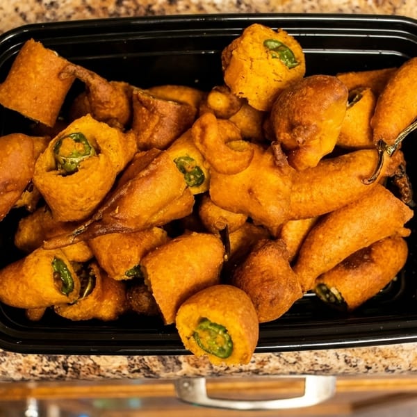 A black container filled with golden-brown, battered chili peppers on a speckled countertop.